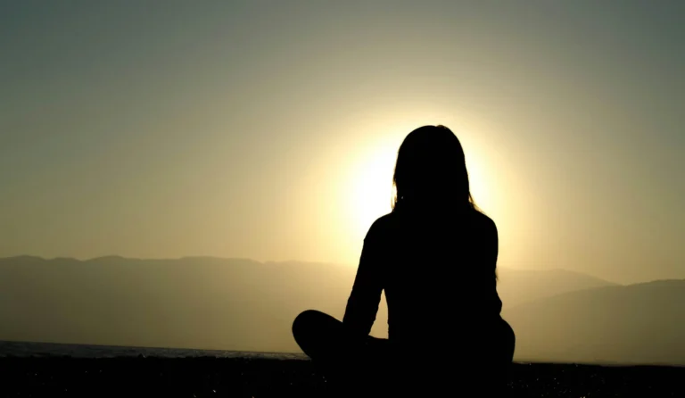 Silhouette of a person meditating at sunrise by the sea – symbolizing stress reduction and liver health connection
